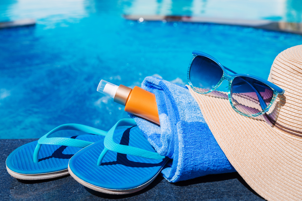 Flip flops, sunblock, towel, sunglasses and sunhat by a pool